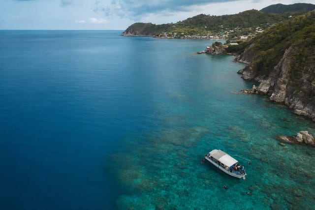 Aerial view of a coastal diving area with turquoise shallows and a dive boat